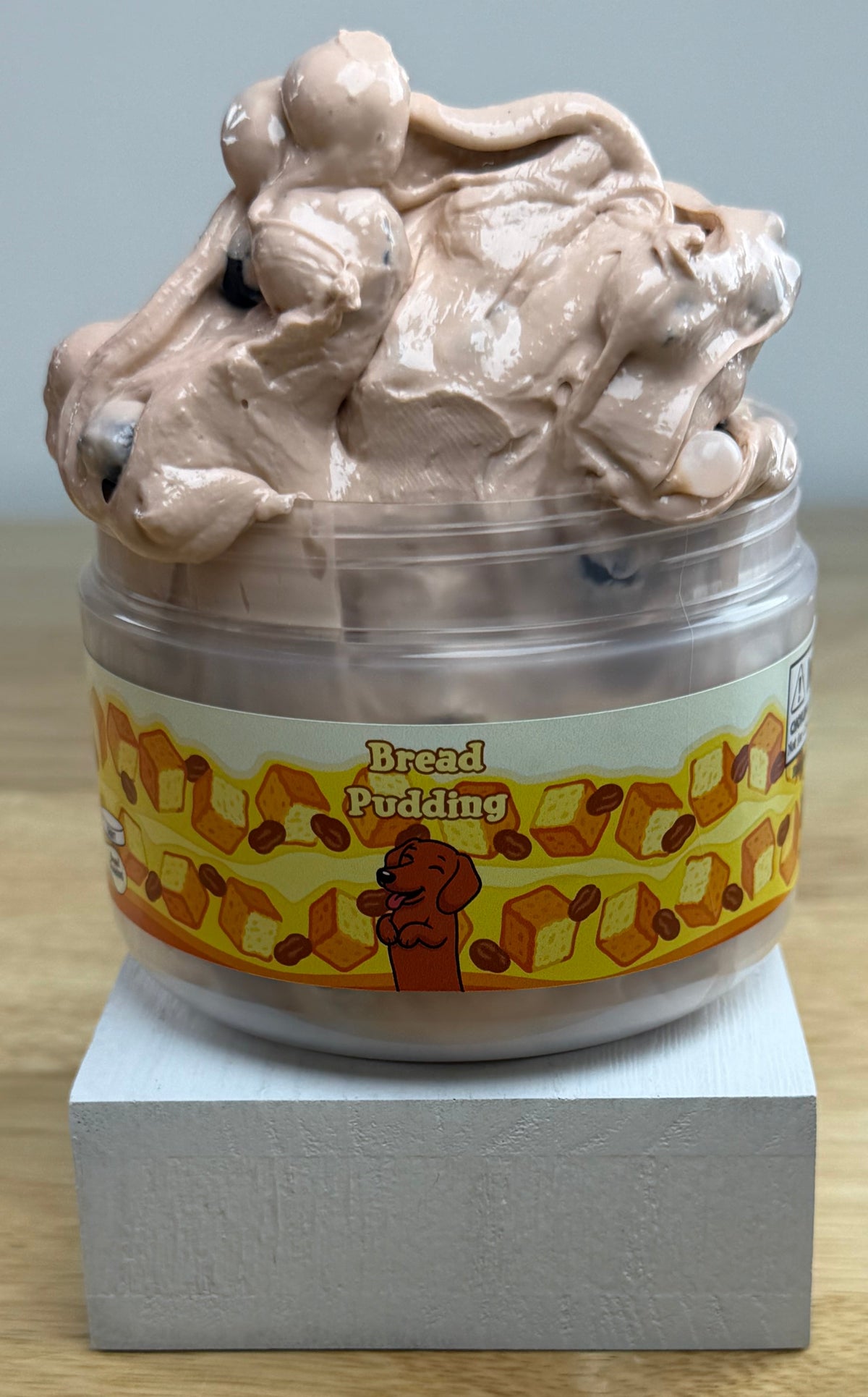 bread pudding tan slime with dark brown pebbles in a clear jar with a bread pudding label with bread raisins and a dog