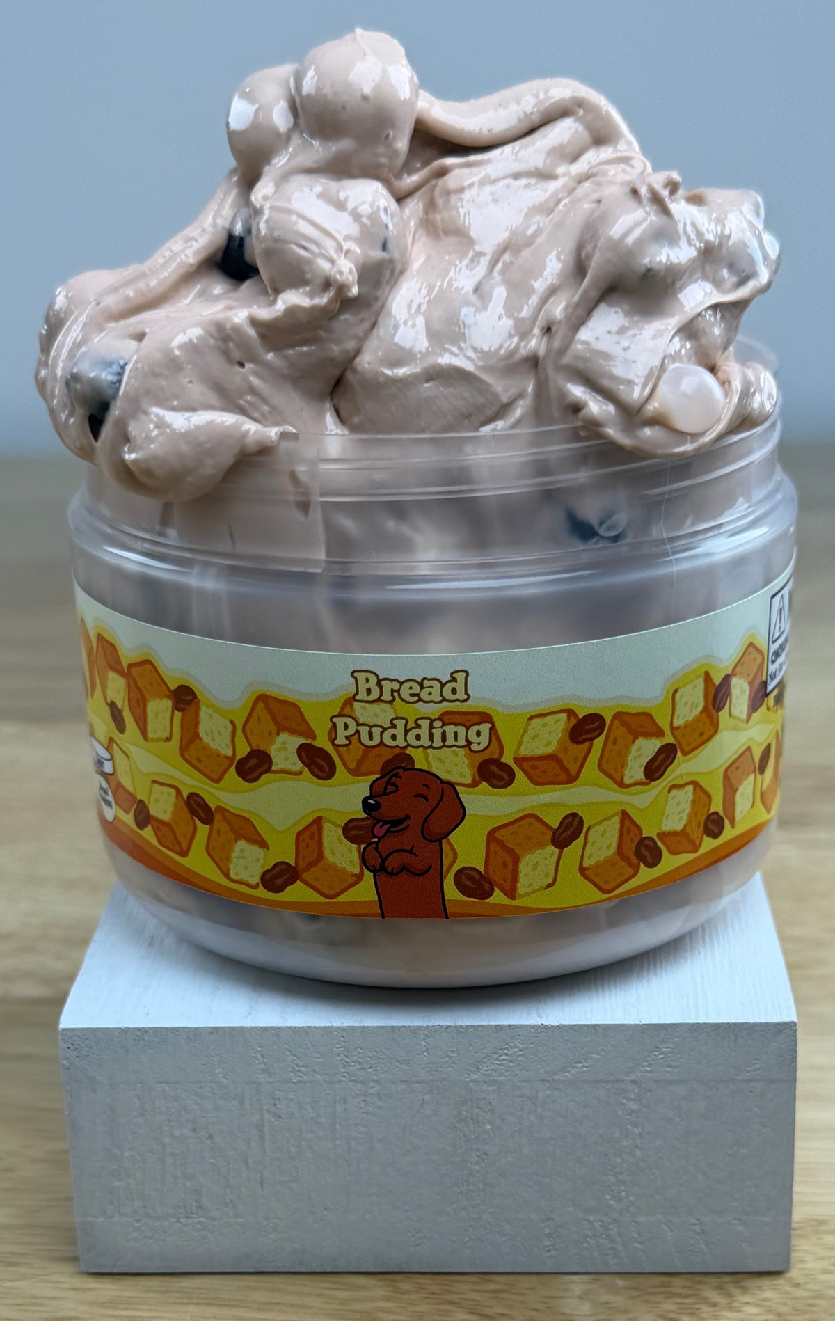 bread pudding tan slime with dark brown pebbles in a clear jar with a bread pudding label with bread raisins and a dog