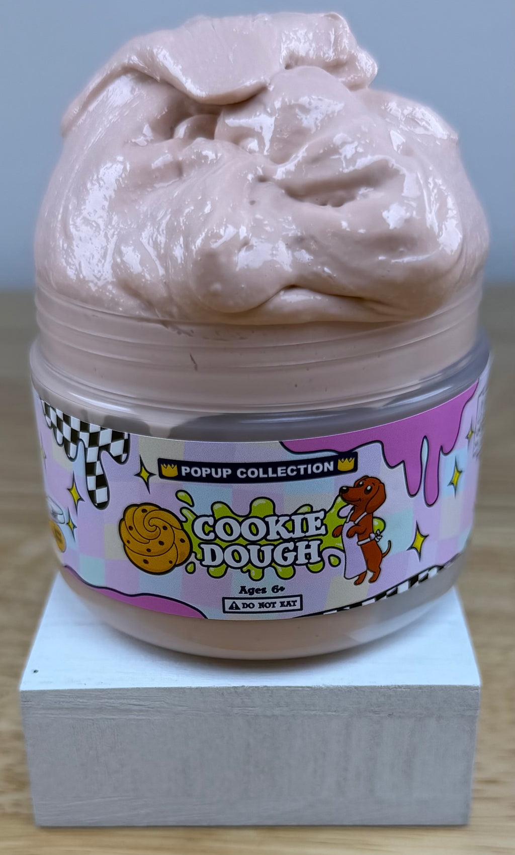 Light tan thick and glossy slime in a plastic jar labelled pop up collection with a dog and a cookie dough logo labelled cookie dough