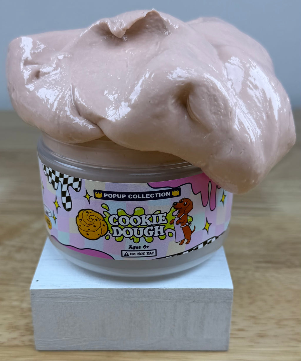 Light tan thick and glossy slime in a plastic jar labelled pop up collection with a dog and a cookie dough logo labelled cookie dough