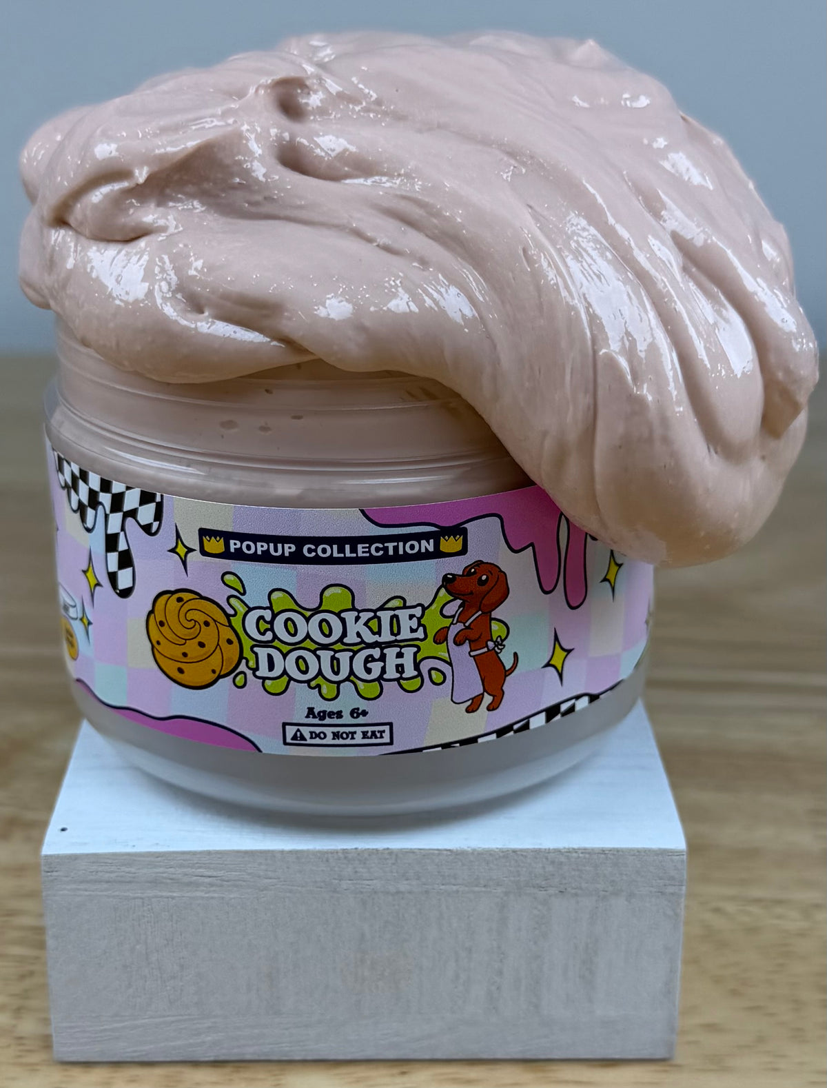 Light tan thick and glossy slime in a plastic jar labelled pop up collection with a dog and a cookie dough logo labelled cookie dough
