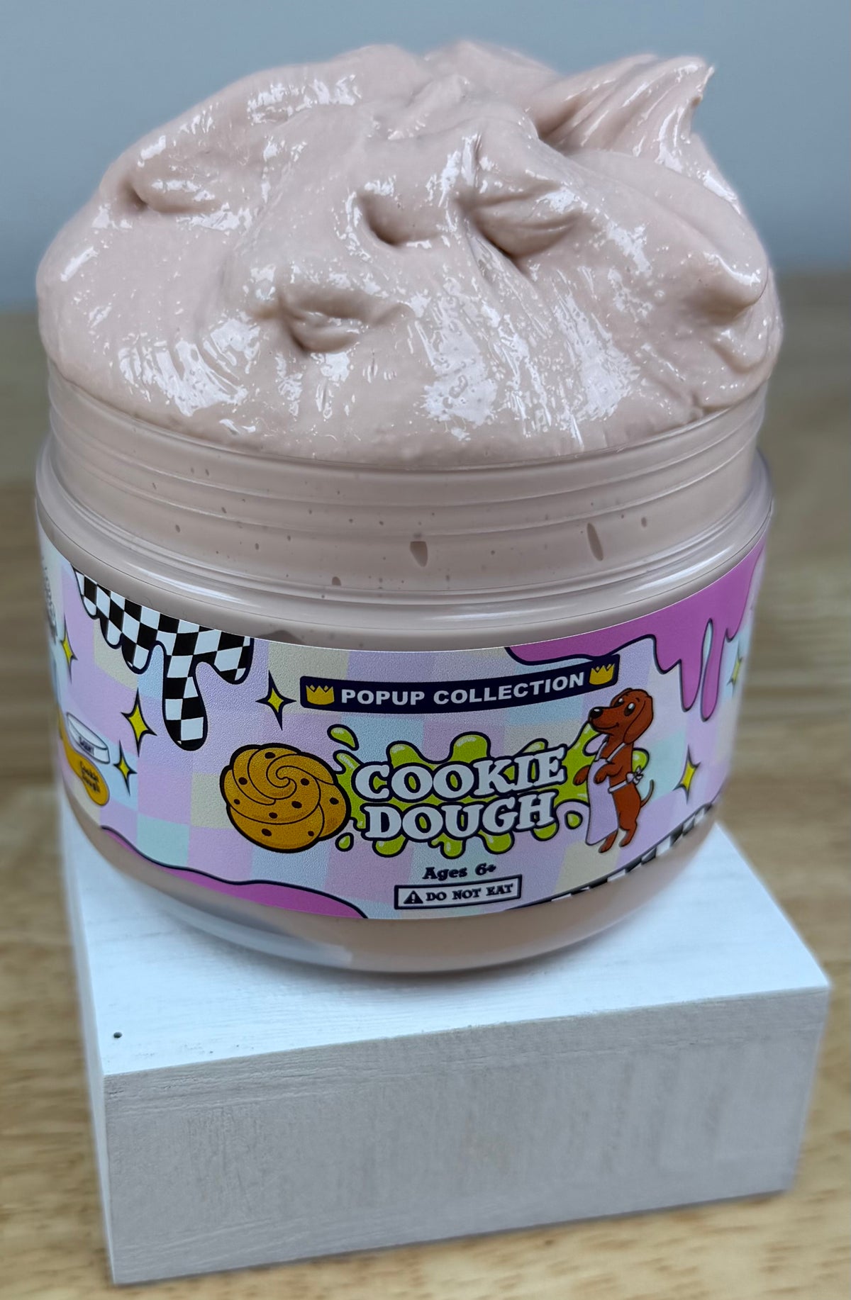 Light tan thick and glossy slime in a plastic jar labelled pop up collection with a dog and a cookie dough logo labelled cookie dough