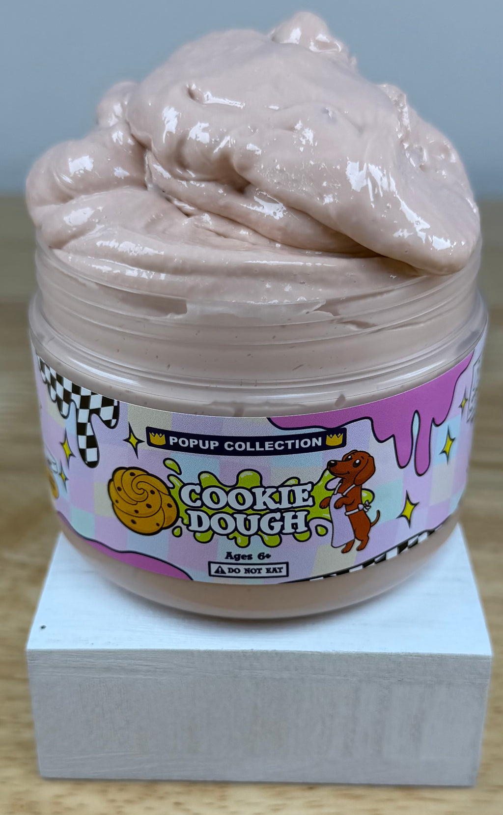 Light tan thick and glossy slime in a plastic jar labelled pop up collection with a dog and a cookie dough logo labelled cookie dough