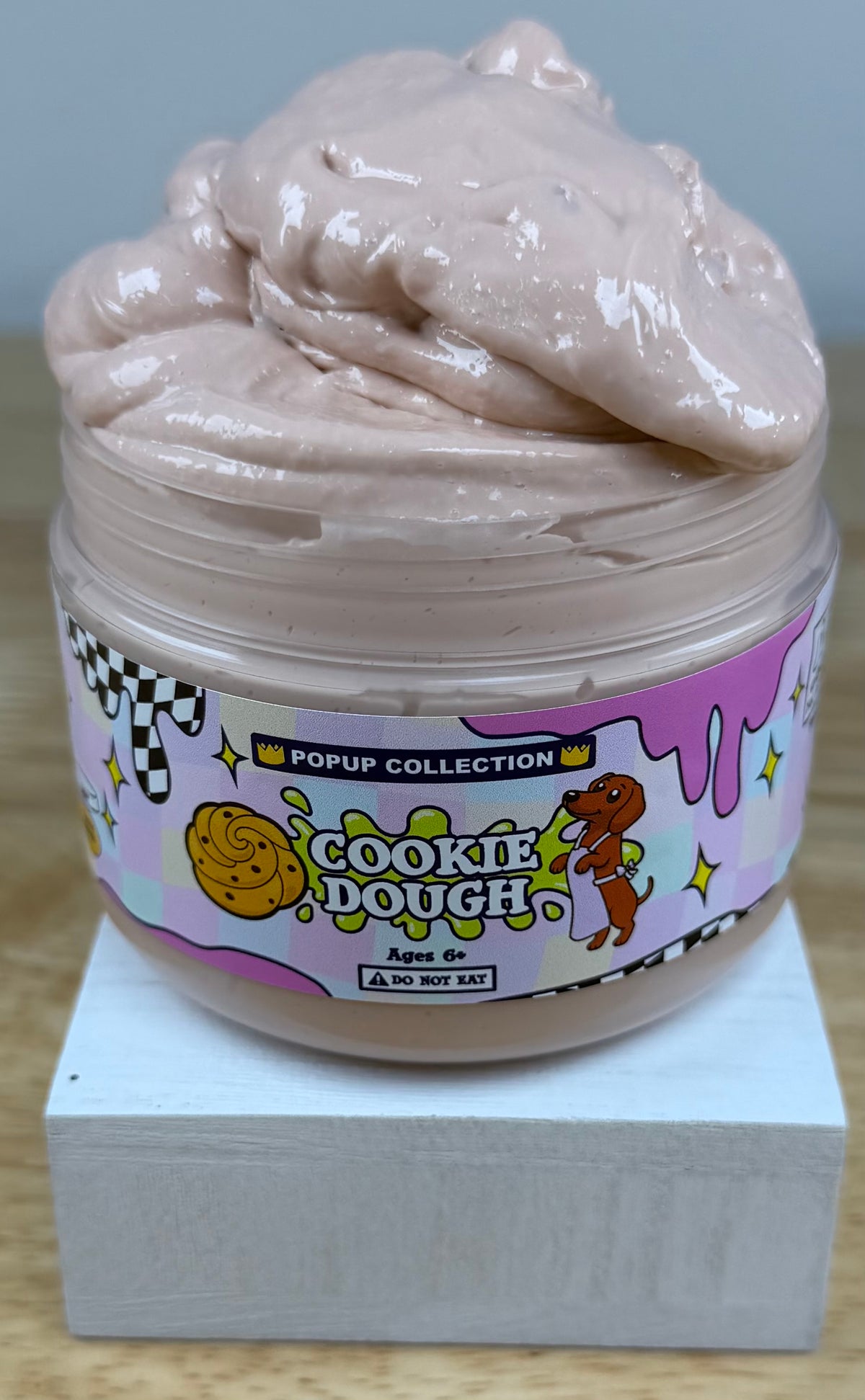 Light tan thick and glossy slime in a plastic jar labelled pop up collection with a dog and a cookie dough logo labelled cookie dough