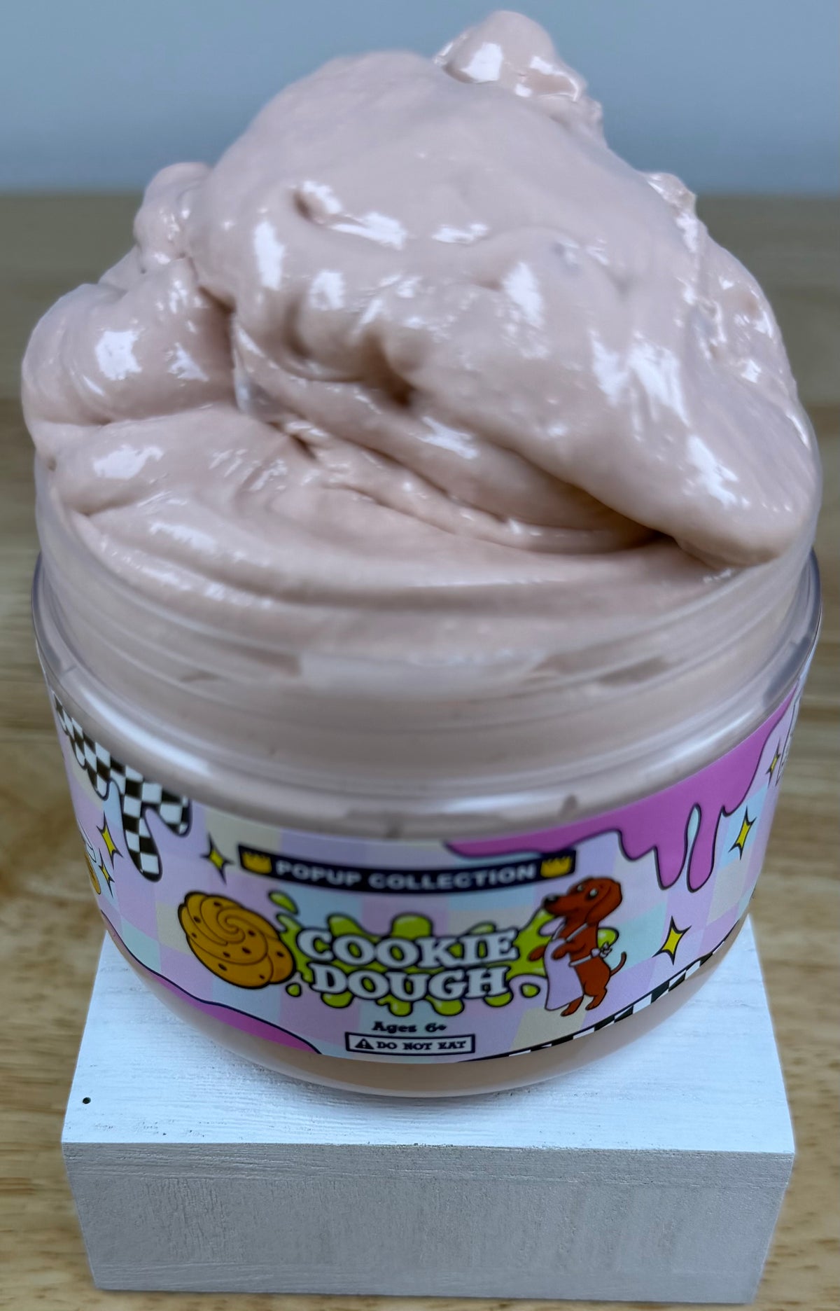 Light tan thick and glossy slime in a plastic jar labelled pop up collection with a dog and a cookie dough logo labelled cookie dough