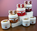 A set of slime jars with colorful labels, arranged on white display blocks over a wooden table against a pink background.