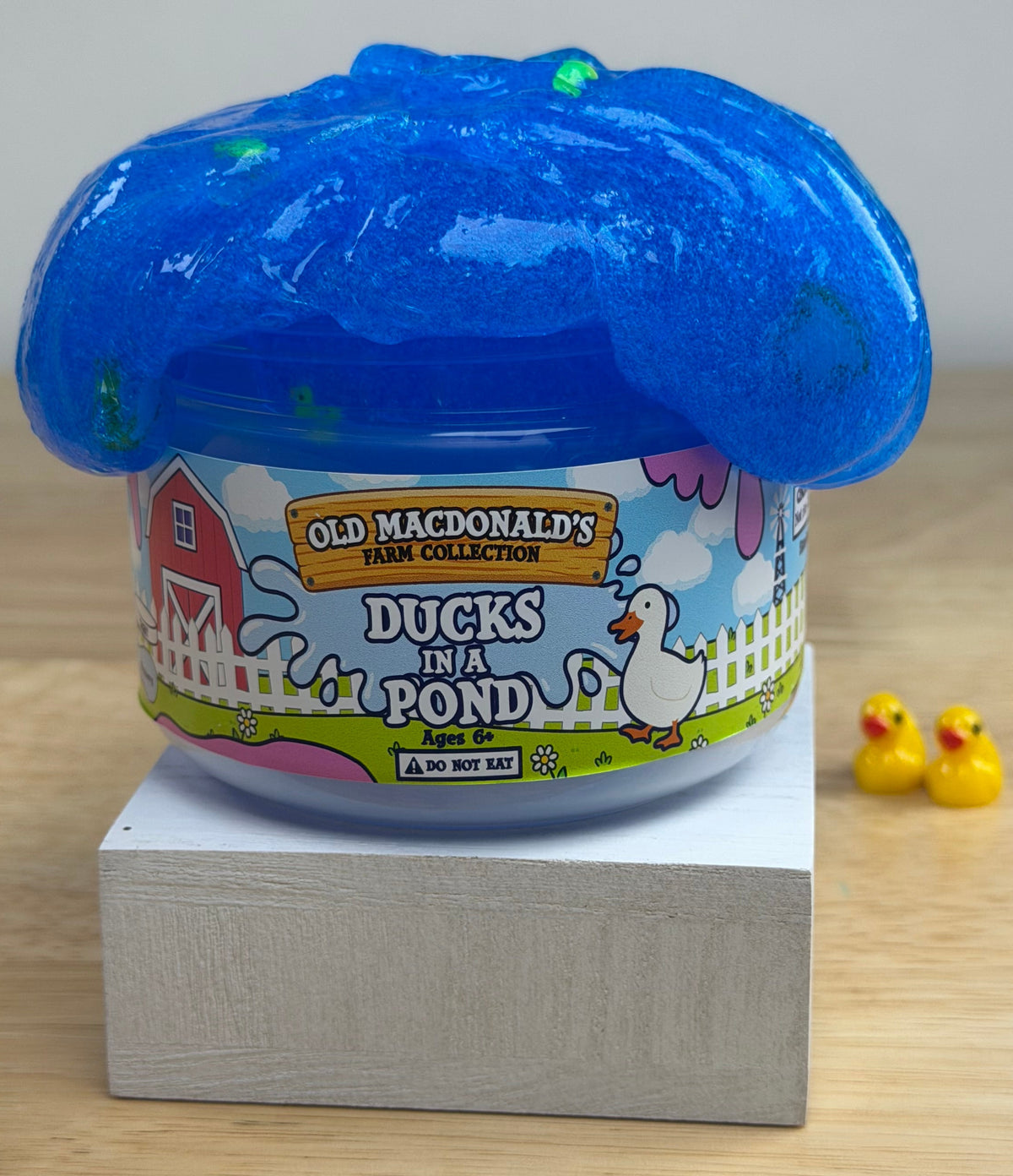 clear blue slime with ducks and bread clay slices in a clear jar with an old macdonald's farm collection ducks on a pond label with a farm background and duck