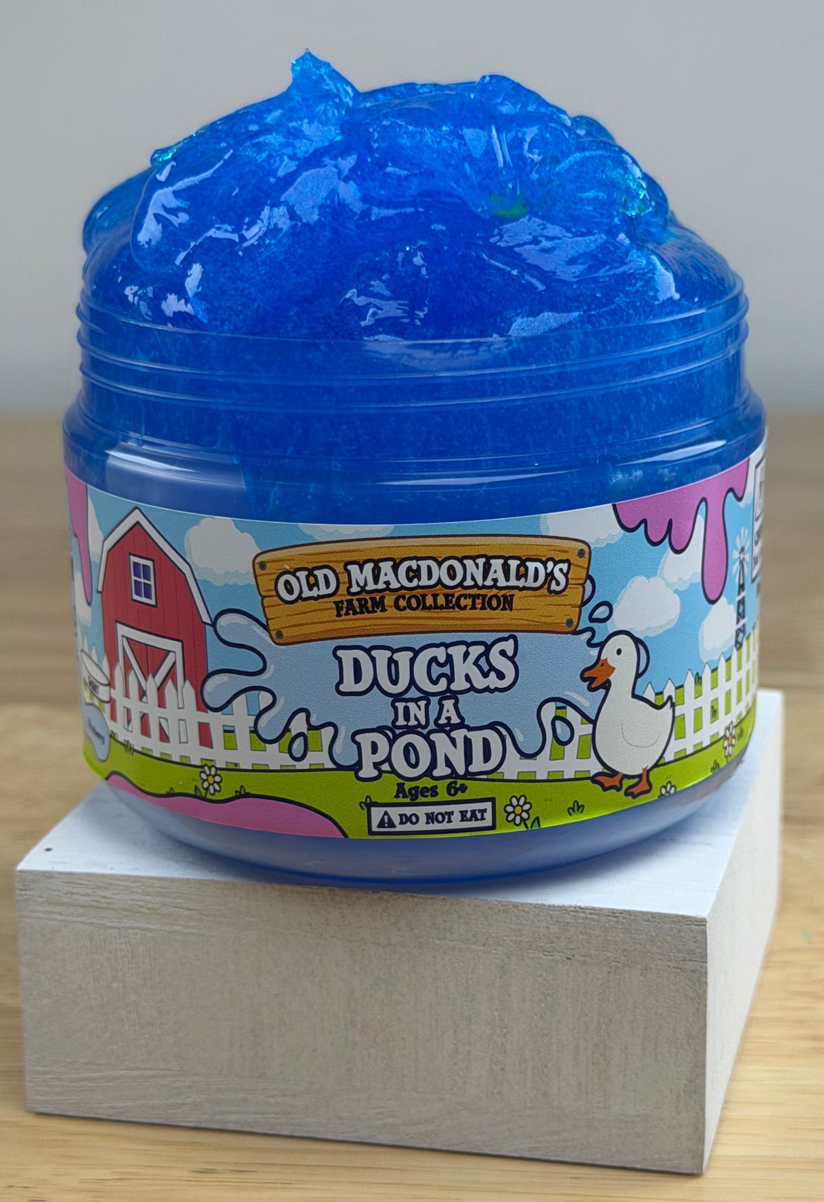 clear blue slime with ducks and bread clay slices in a clear jar with an old macdonald's farm collection ducks on a pond label with a farm background and duck