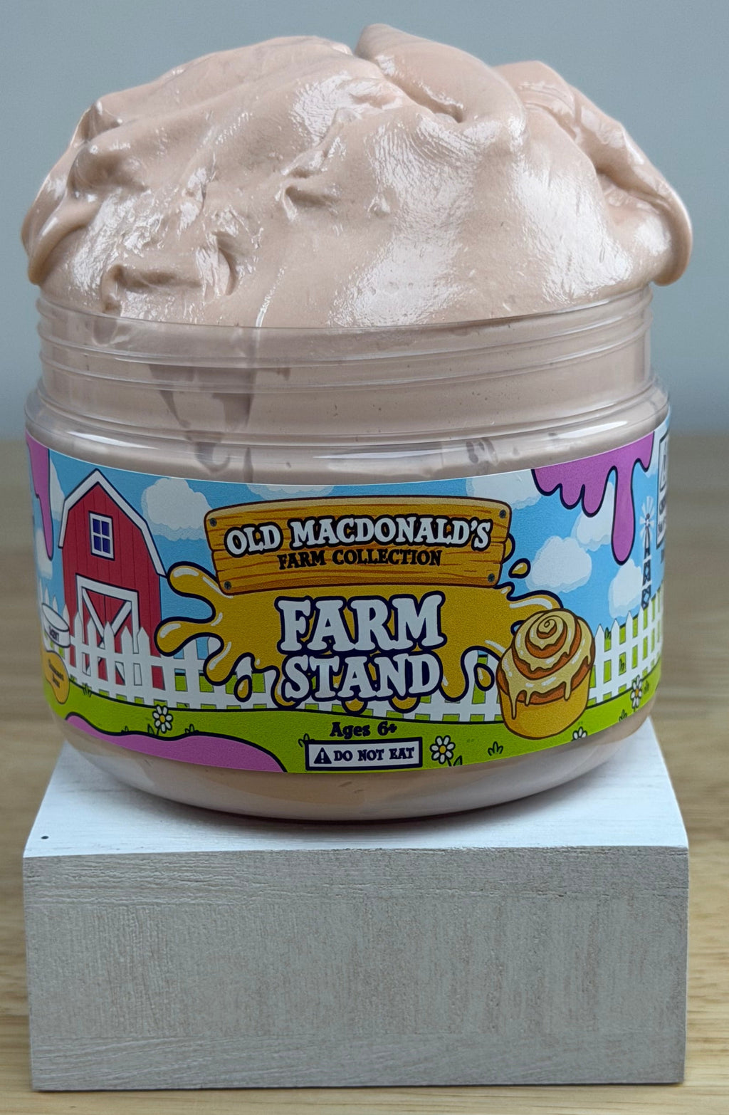 light tan slime in a clear jar with an old macdonald farm collection farm label that says farm stand with a cinnamon roll on it