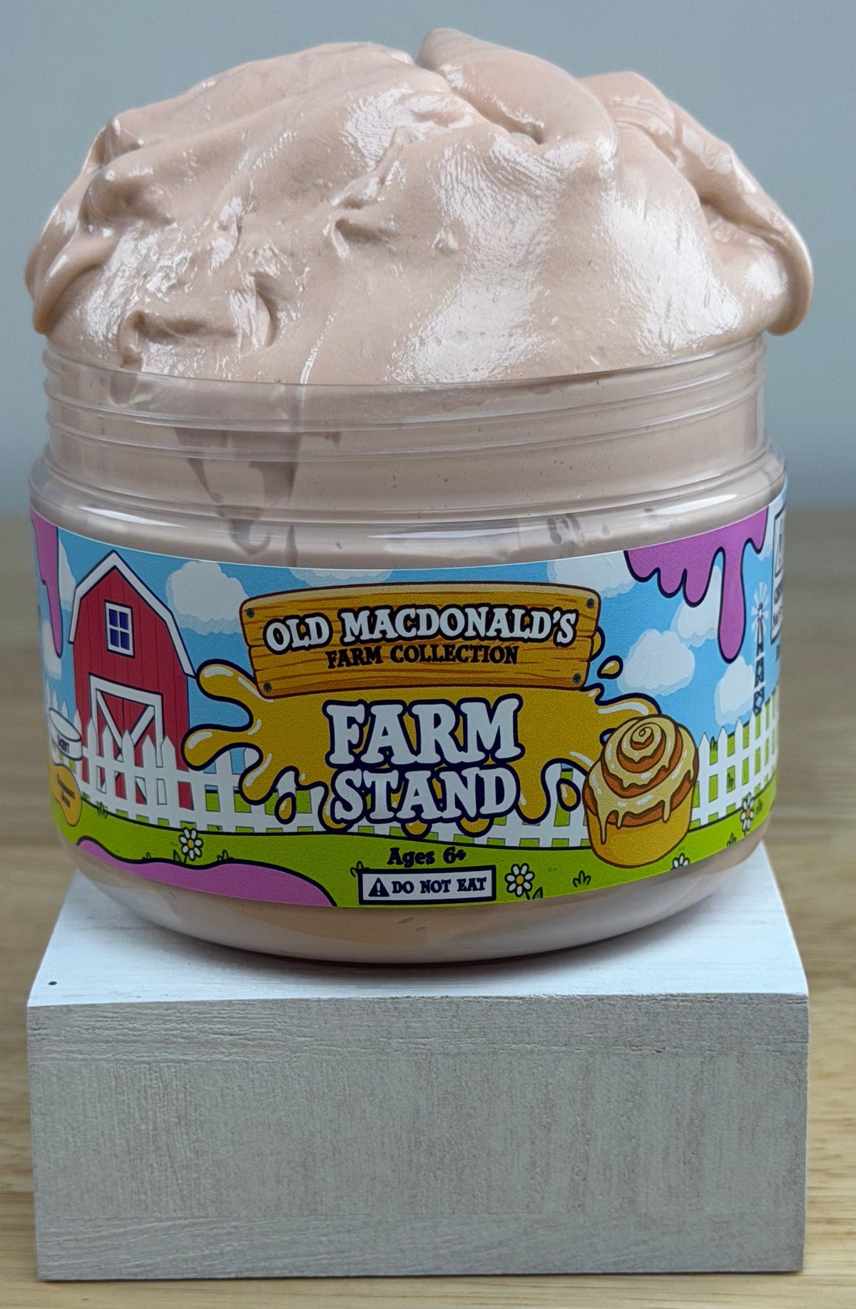light tan slime in a clear jar with an old macdonald farm collection farm label that says farm stand with a cinnamon roll on it