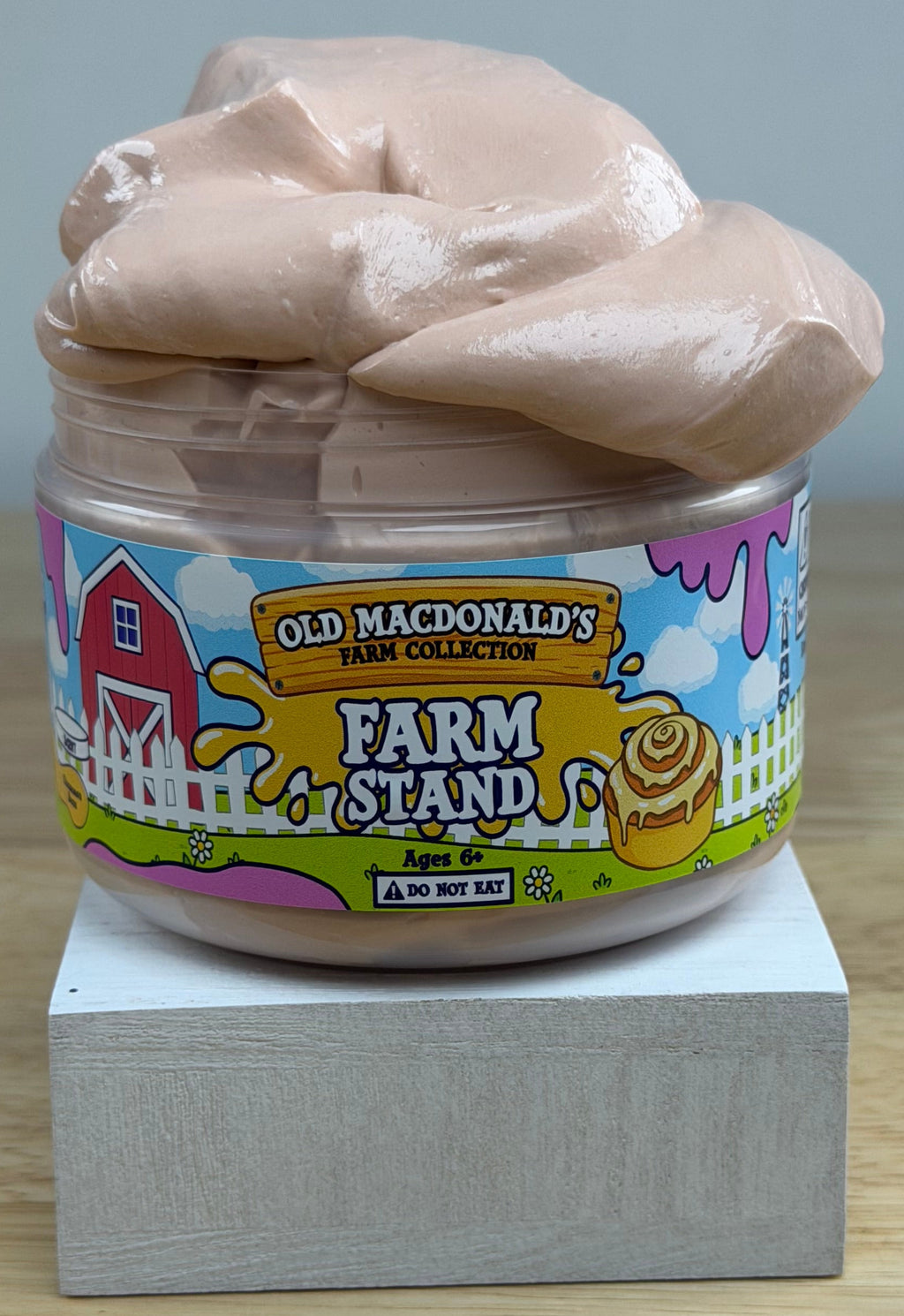 light tan slime in a clear jar with an old macdonald farm collection farm label that says farm stand with a cinnamon roll on it