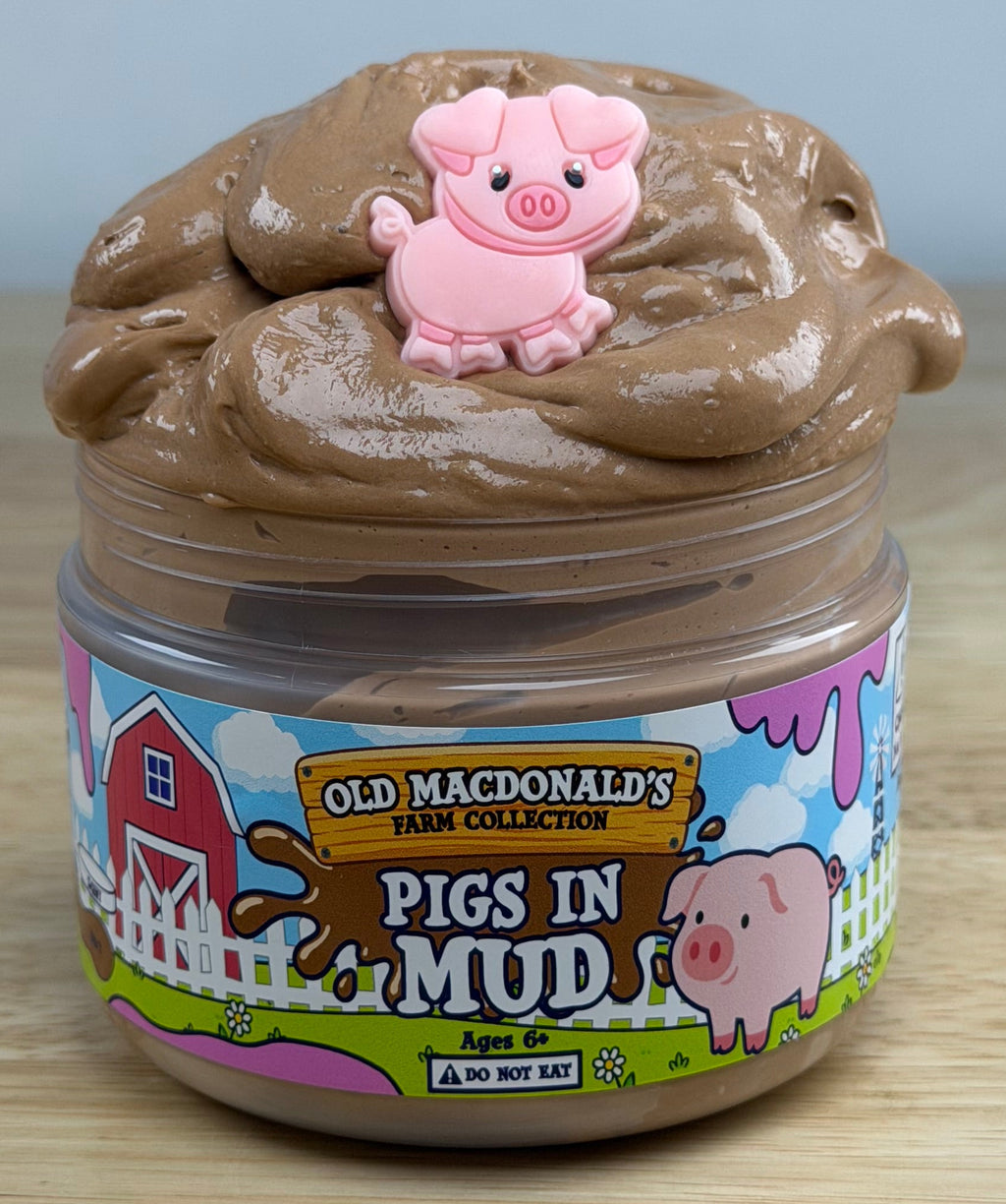 brown slime with a pig charm in a clear jar with an old macdonald farm collection farm label with a pig on it