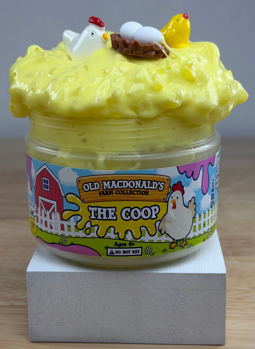 yellow slime with silica in a clear jar with a farm label that says old macdonald's farm collection the coop with a chicken topped with a chicken basket two eggs and a baby chicken