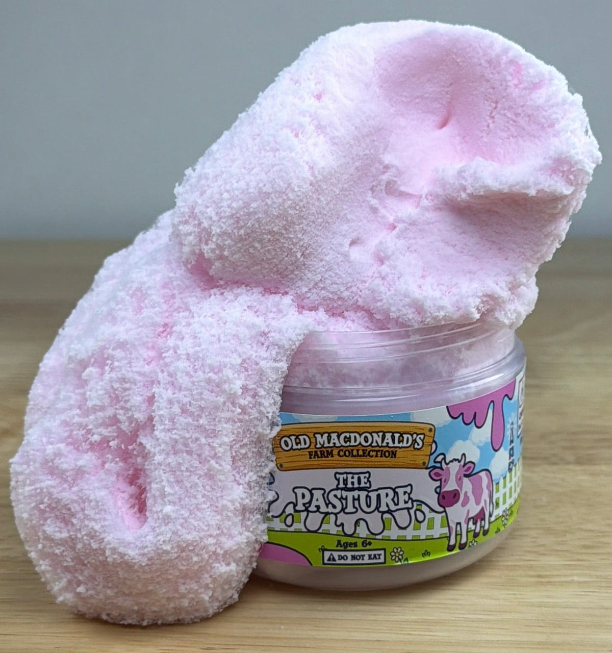 white and pink cloud slime with a cow charm in a clear jar with an old macdonald farm label with a cow that says the pasture