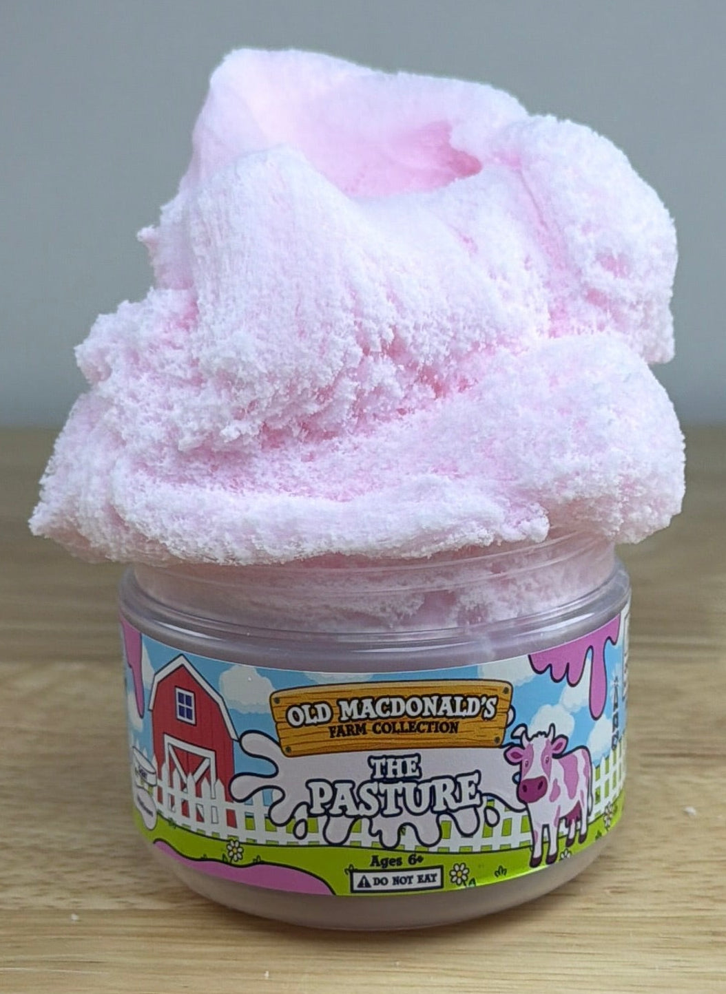 white and pink cloud slime with a cow charm in a clear jar with an old macdonald farm label with a cow that says the pasture