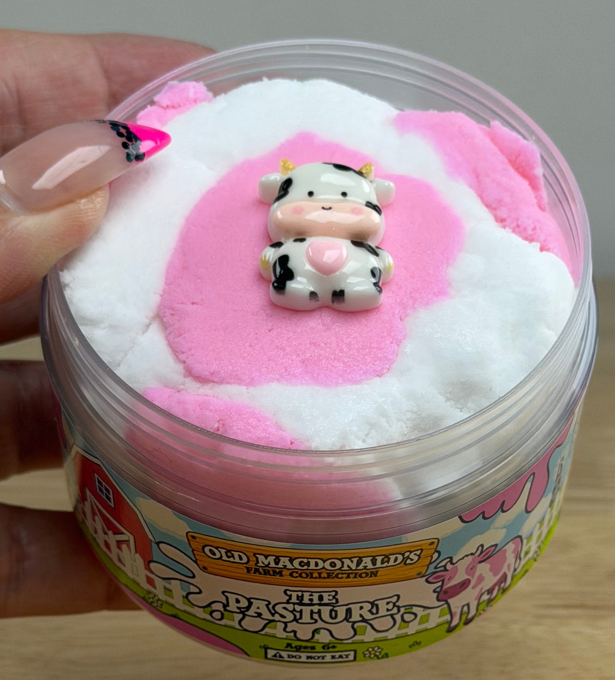 white and pink cloud slime with a cow charm in a clear jar with an old macdonald farm label with a cow that says the pasture