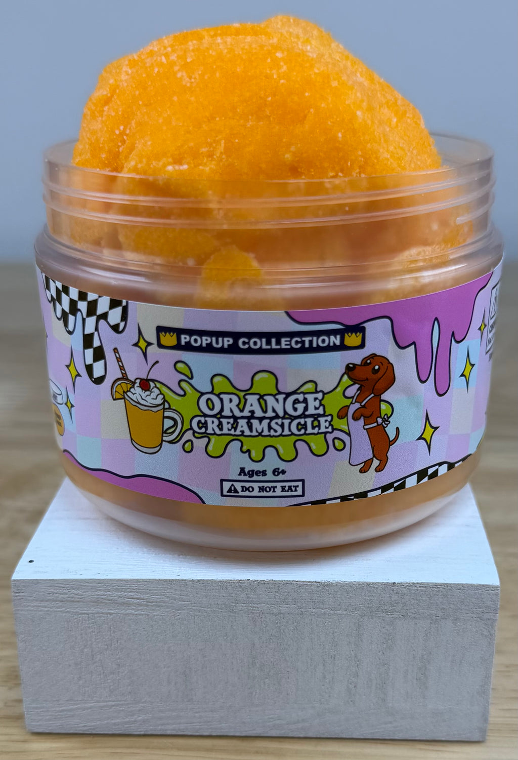 Orange cloud slime in a pop up collection labelled plastic jar that says orange creamsicle with a dog and a cup with orange dessert in it.