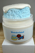 A novelty jar of 'Wonderland' slime, featuring a plastic jar with a white and light blue label, topped with light blue clay cake with a white slime drizzle, displayed on a white block.