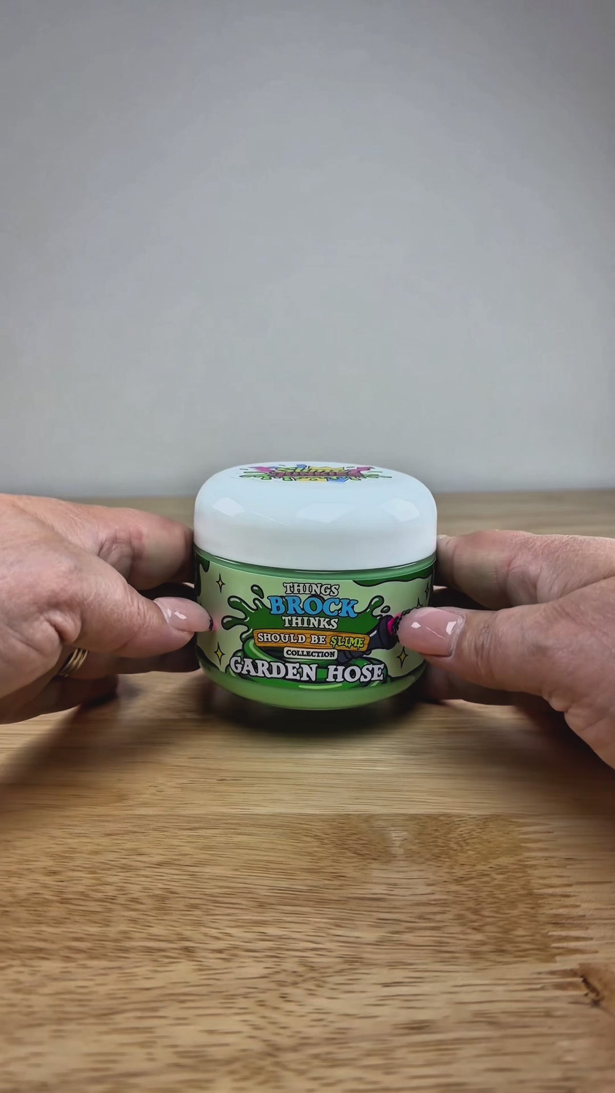 A jar of green slime with a matching green slime mound on top, displayed on a white block over a wooden surface against a white background. The label reads 'Things Brock Thinks Should Be Slime Collector's Edition Garden Hose'.