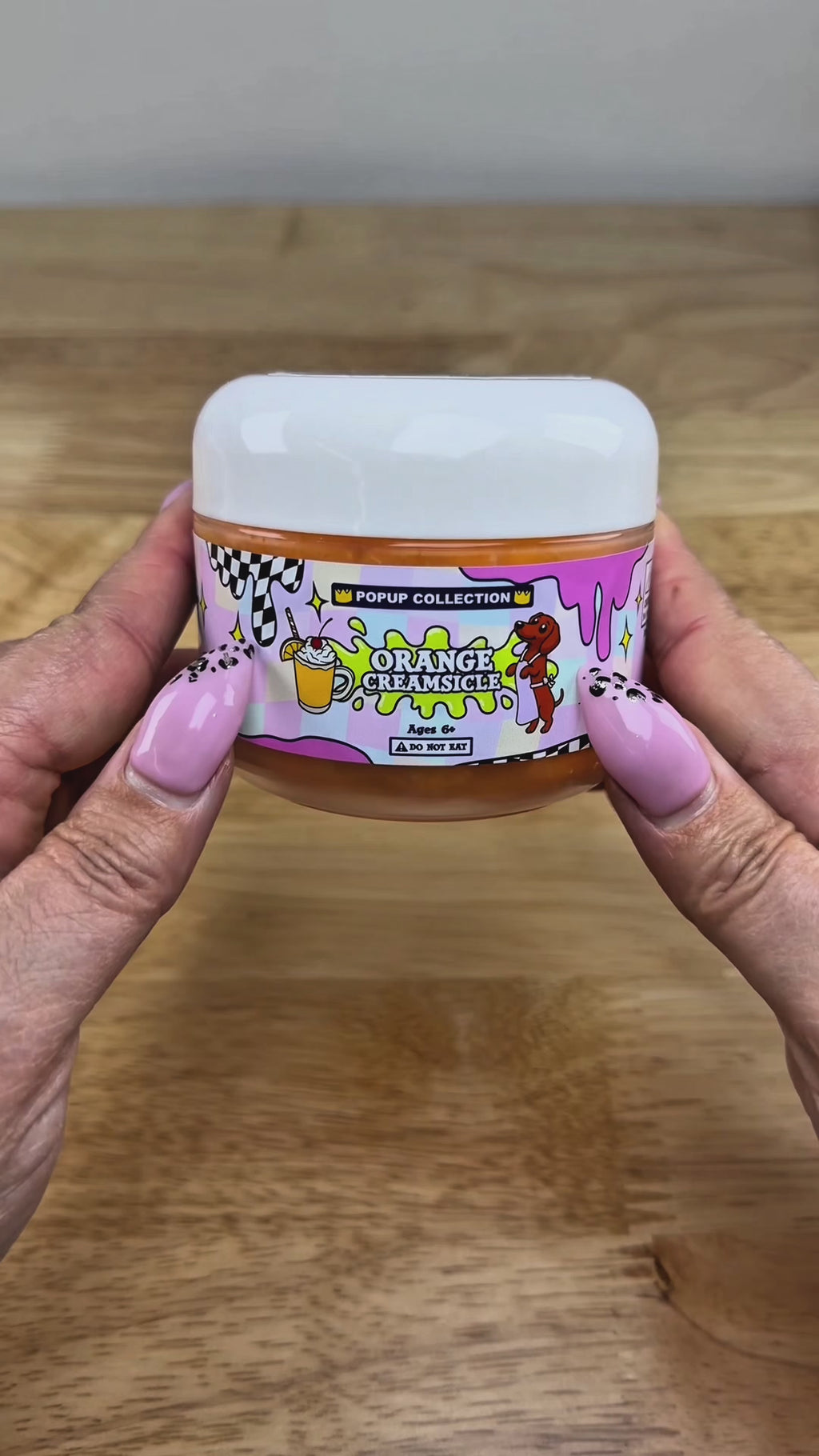 Orange cloud slime in a pop up collection labelled plastic jar that says orange creamsicle with a dog and a cup with orange dessert in it.