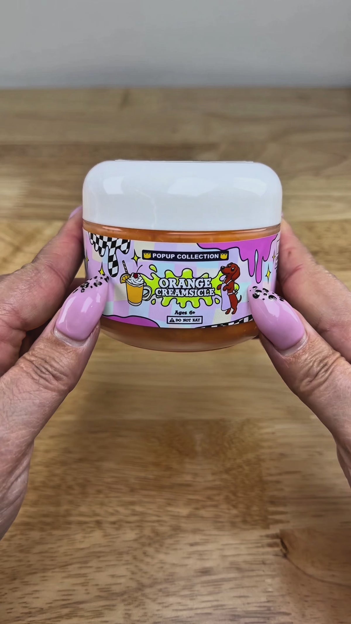 Orange cloud slime in a pop up collection labelled plastic jar that says orange creamsicle with a dog and a cup with orange dessert in it.