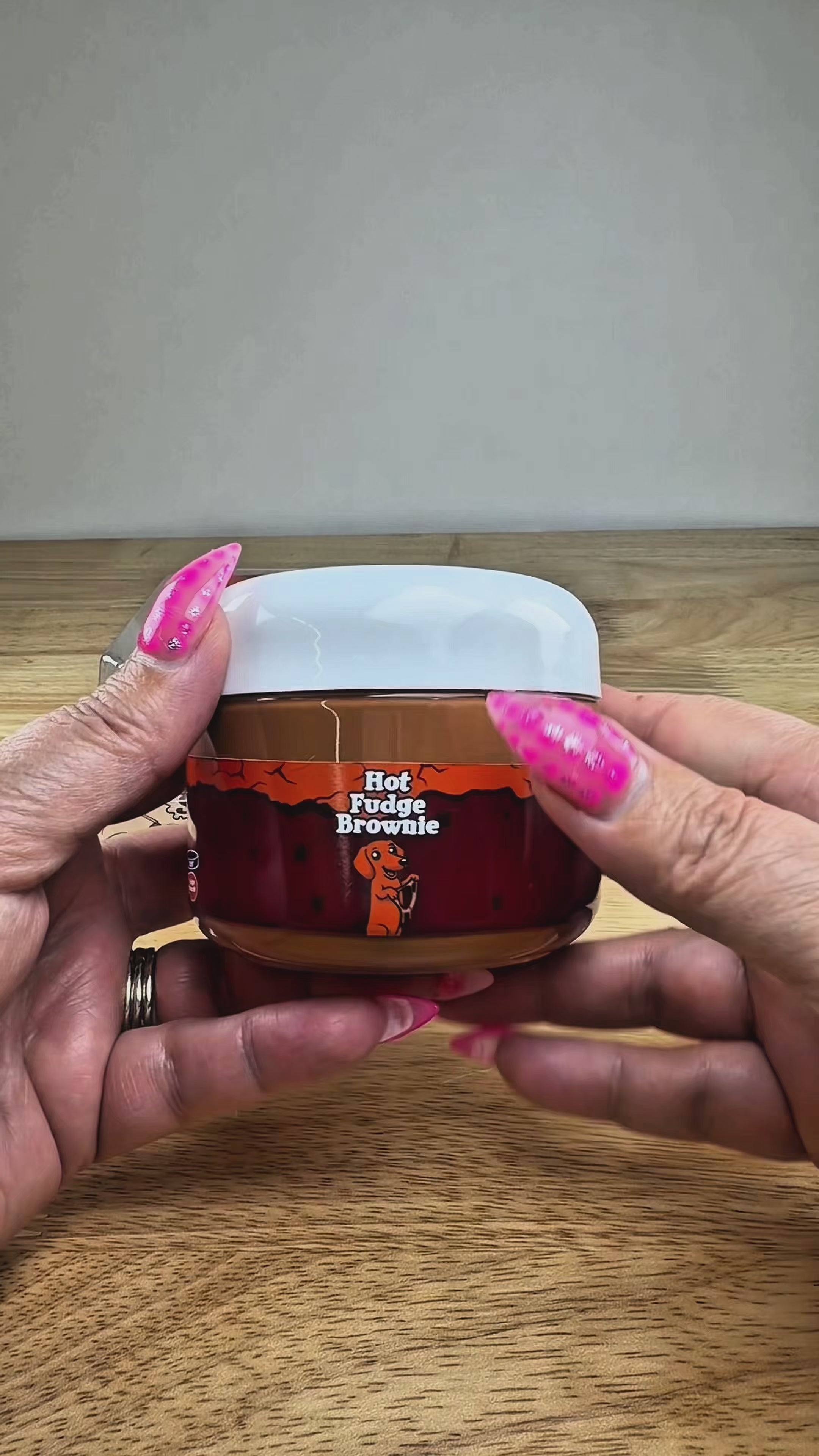 A novelty jar of 'Hot Fudge Brownie' slime, featuring a plastic jar with a brown label, topped with brown clay brownie with a brown slime drizzle, displayed on a white block.