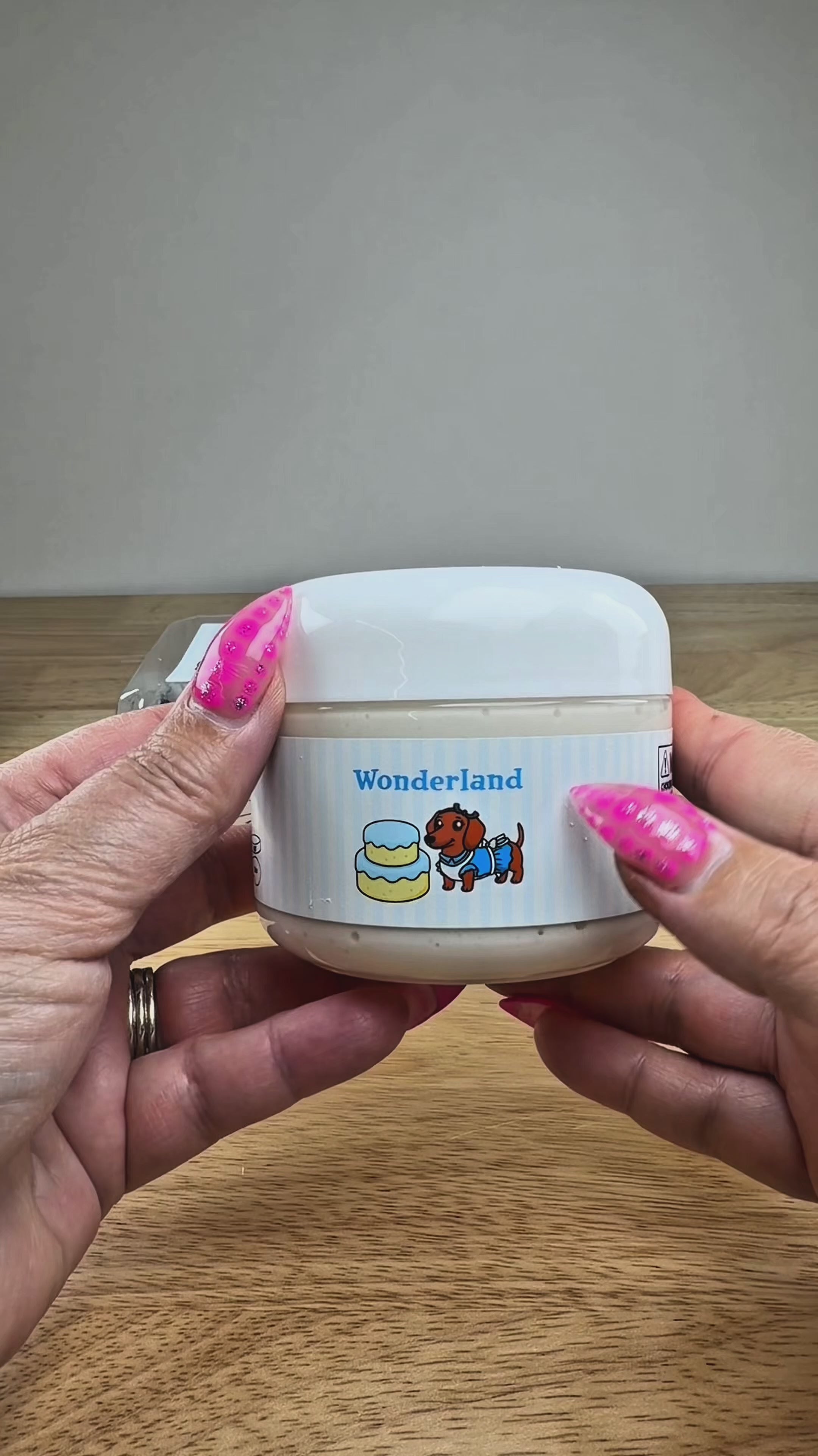 A novelty jar of 'Wonderland' slime, featuring a plastic jar with a white and light blue label, topped with light blue clay cake with a white slime drizzle, displayed on a white block.